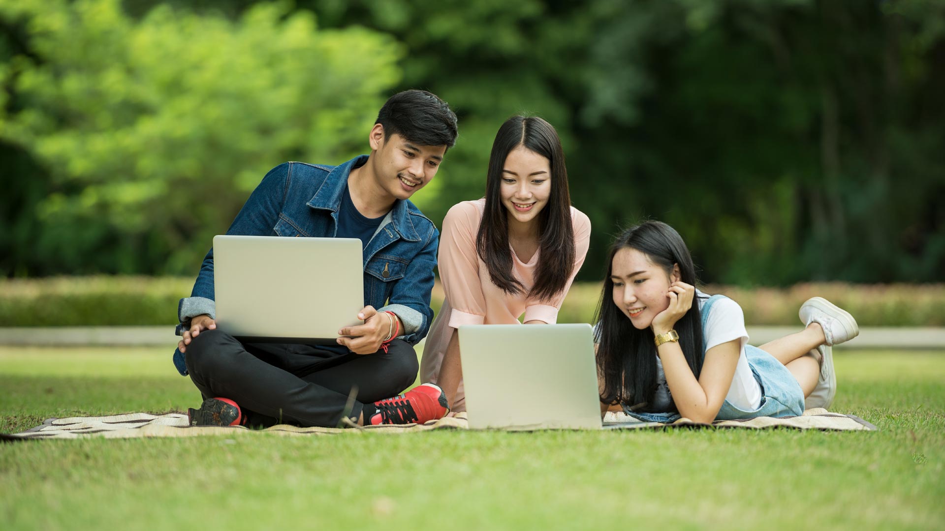 Three teenagers in park on laptops