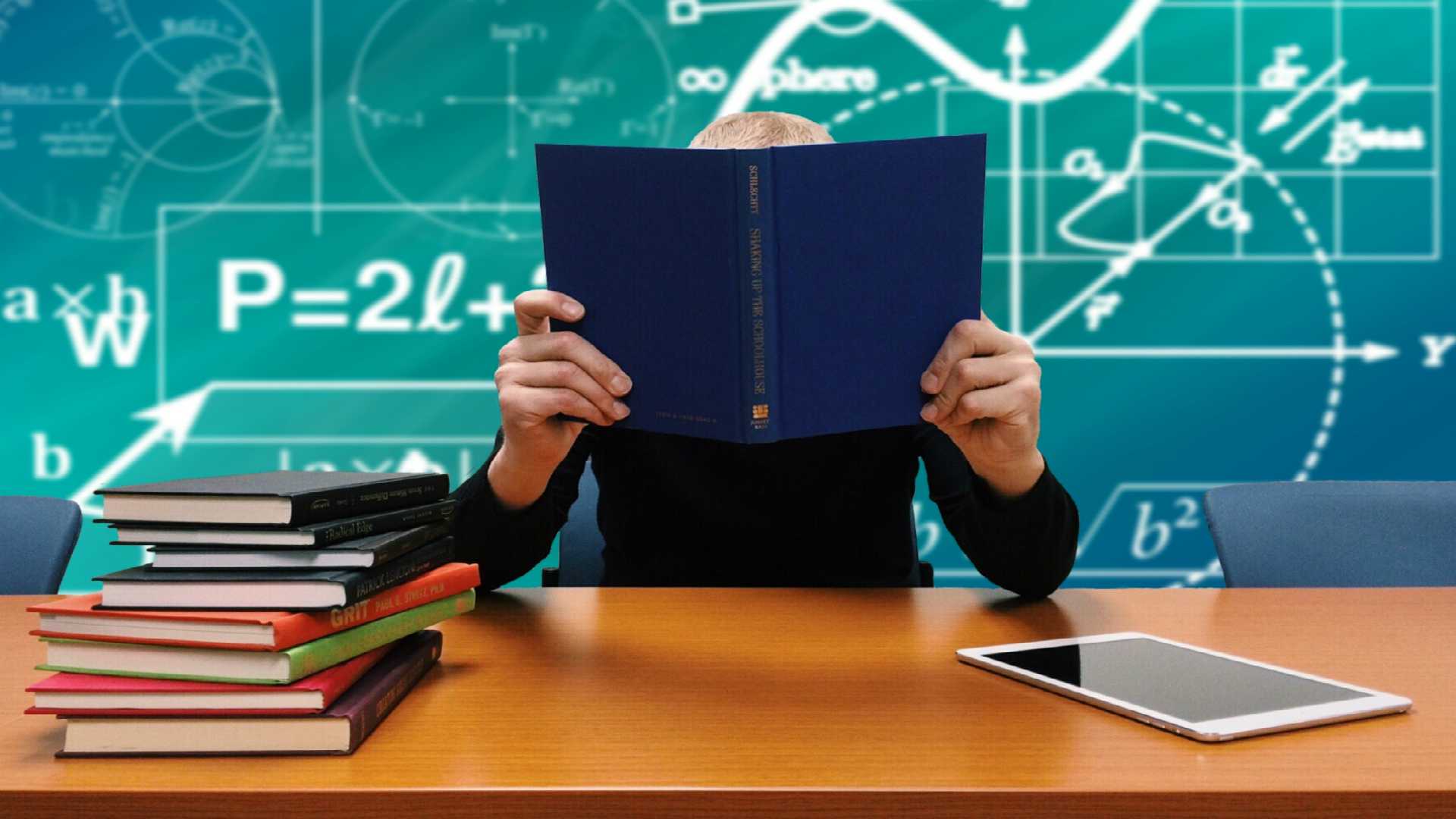 person behind a book with formulas on a chalkboard