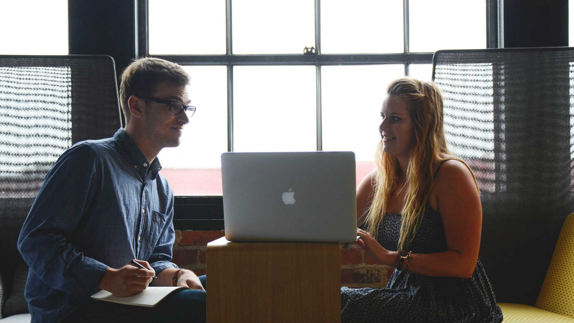 two young people talking with a laptop