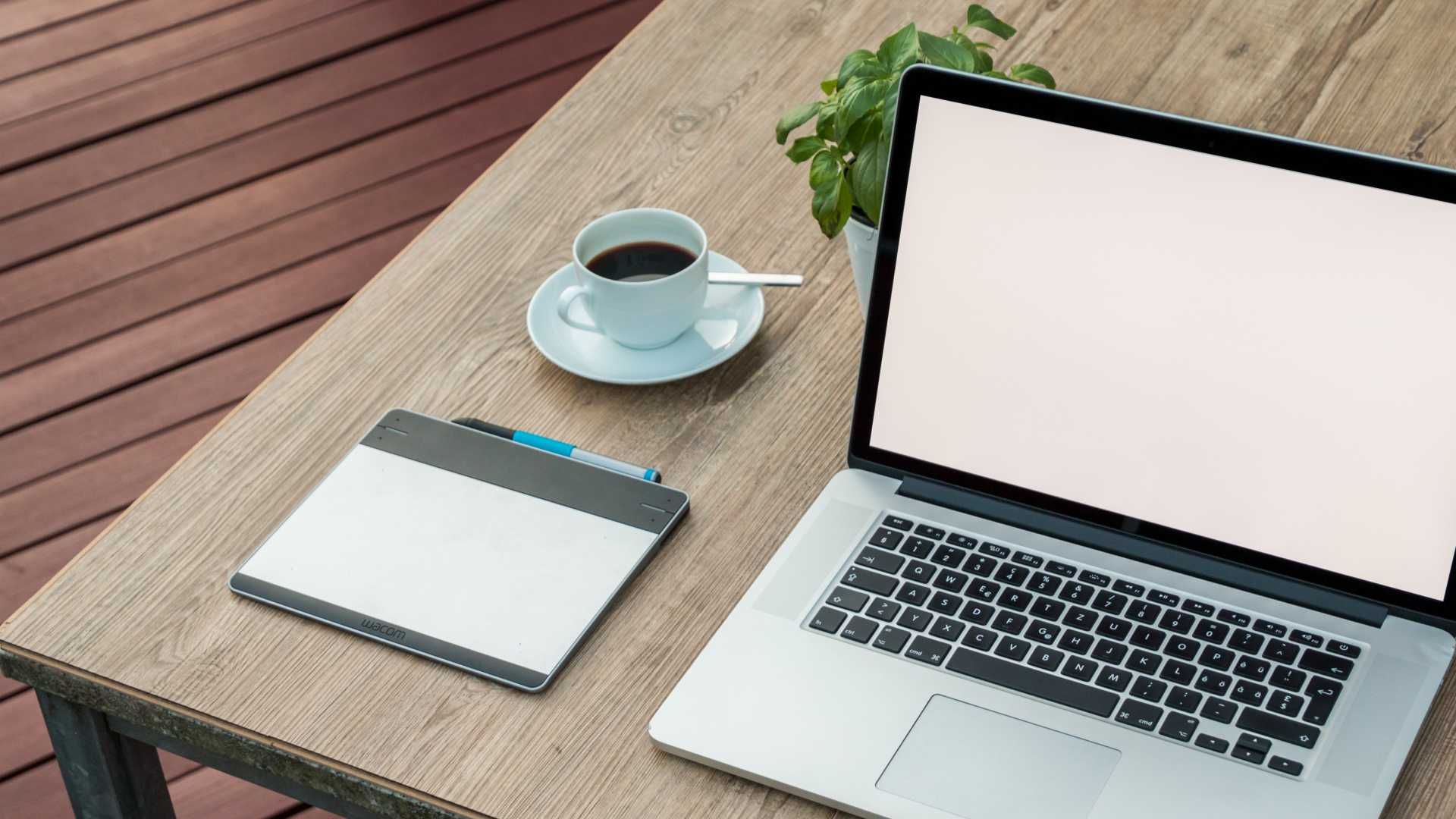 laptop on a table with a notepad, cup of coffee and plant