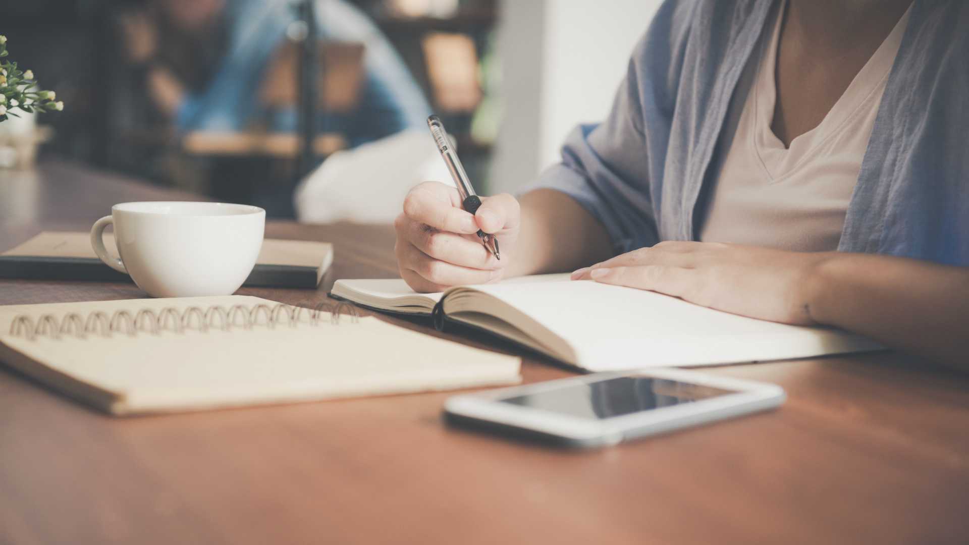 woman writing in a notebook with a smartphone