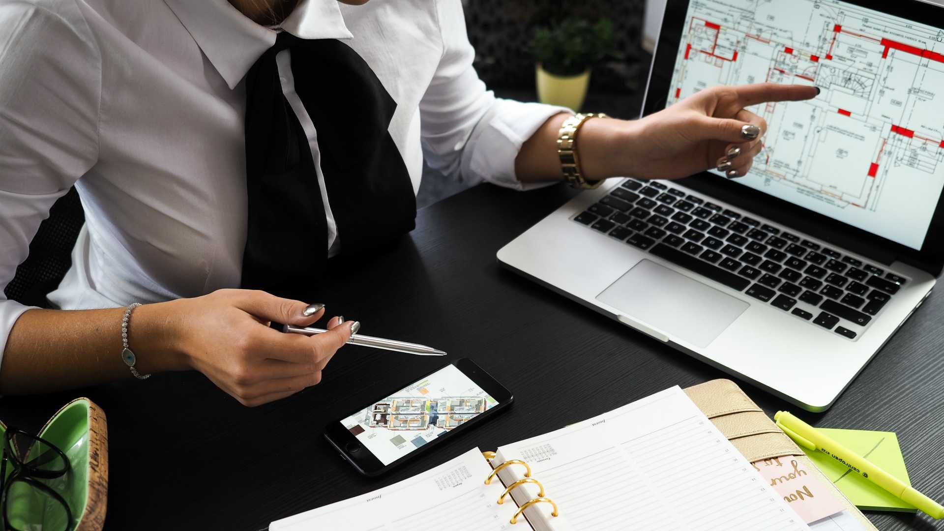 woman at a desk pointing to a laptop