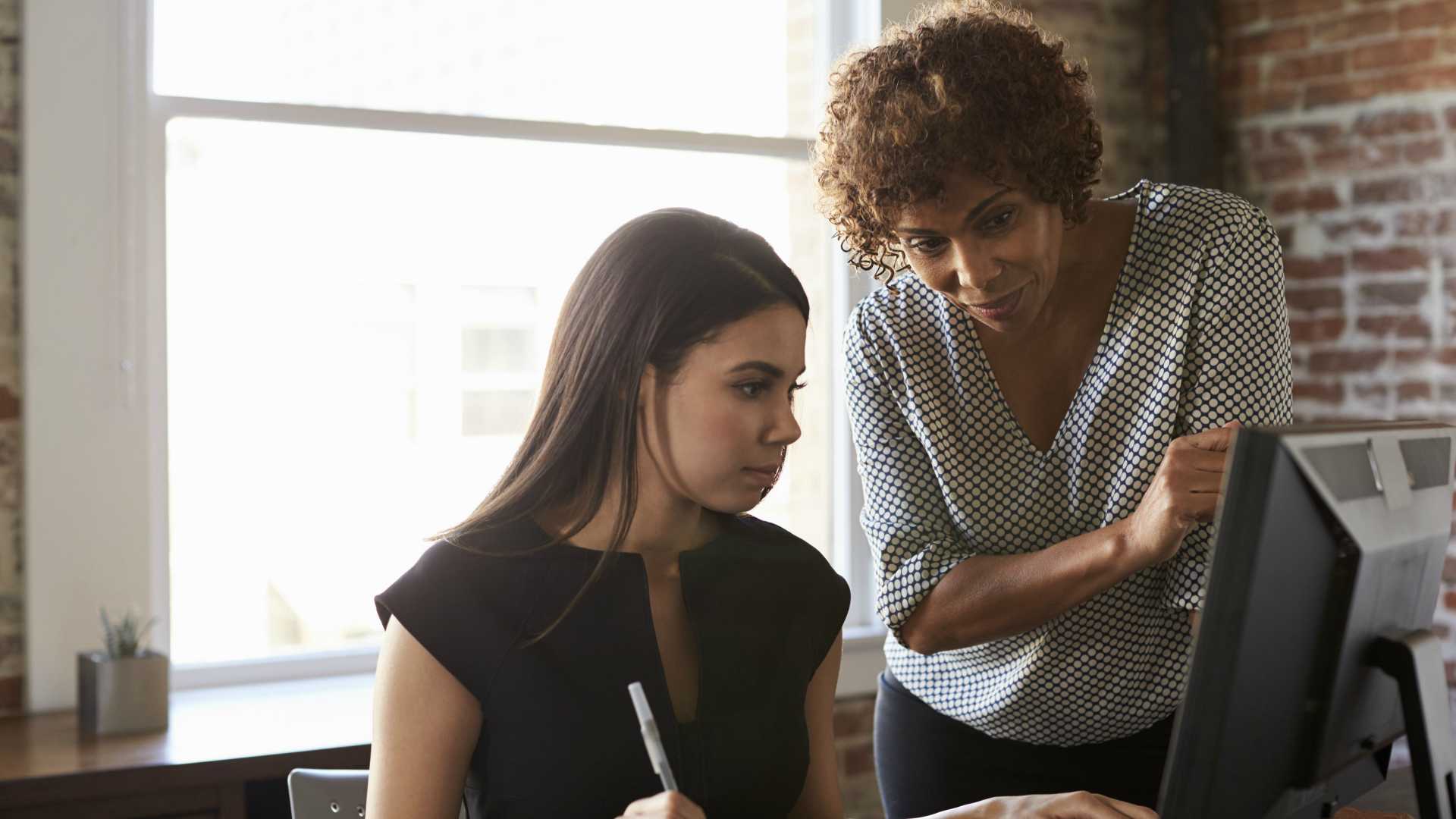 woman helping another woman on a computer