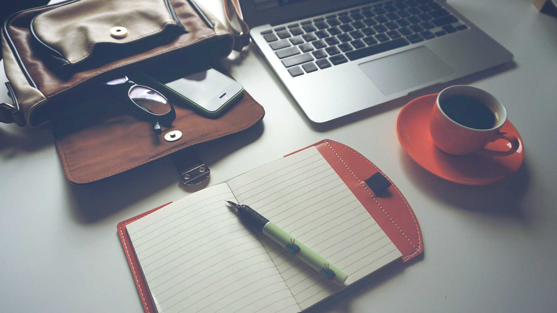 desk with laptop, notebook and pen, coffee, briefcase, phone
