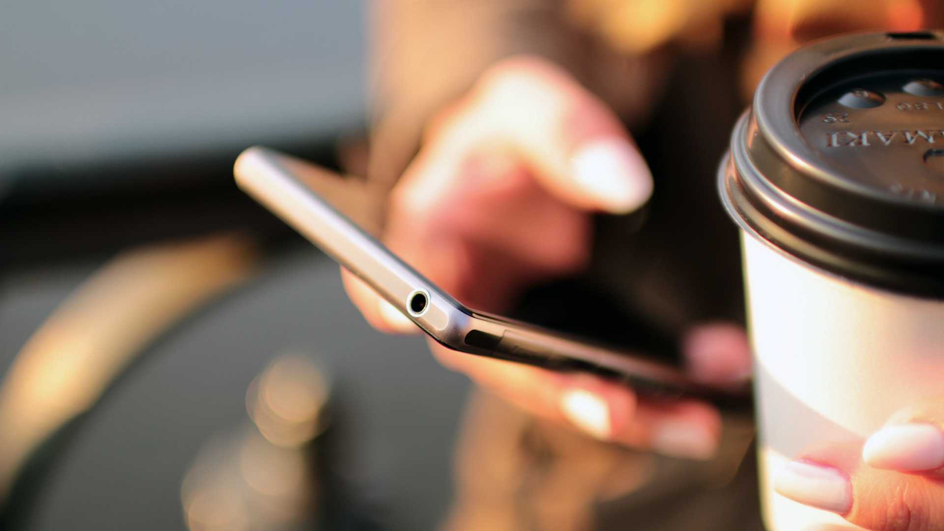 woman using a phone and holding coffee