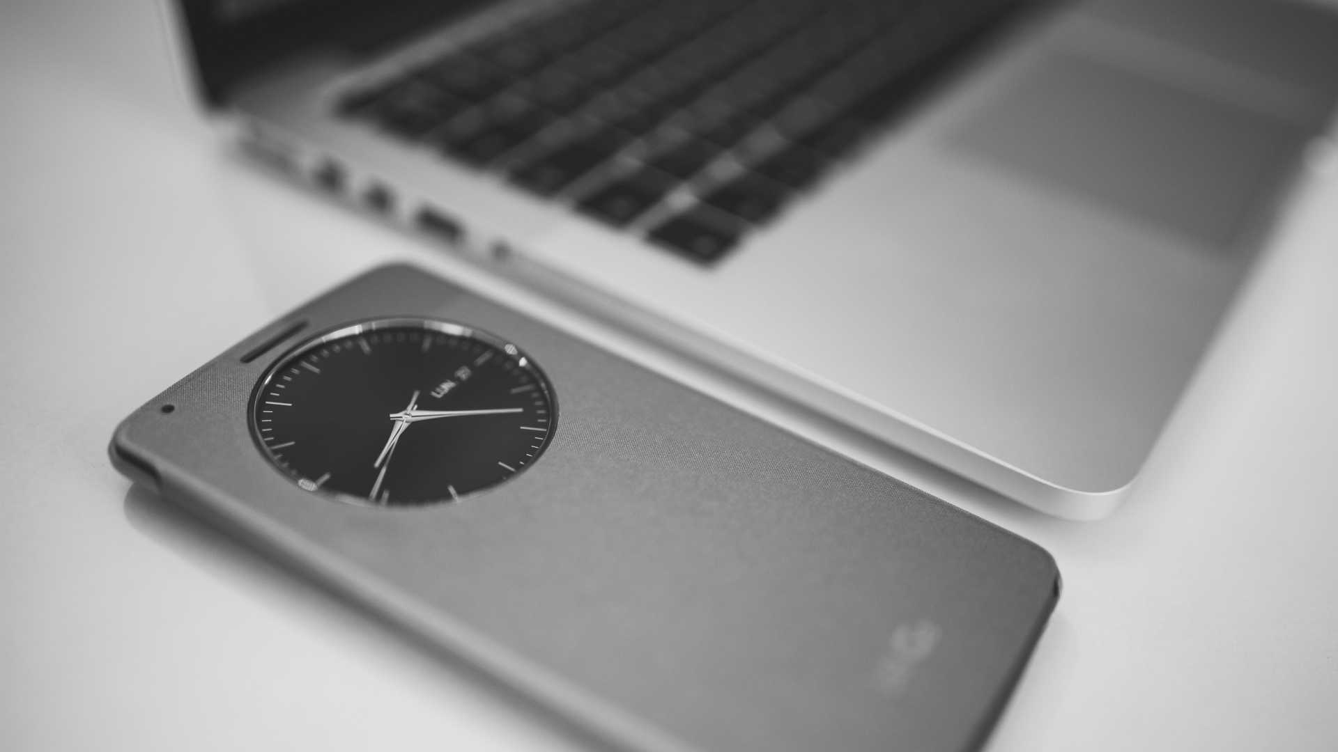 clock on mobile phone next to laptop