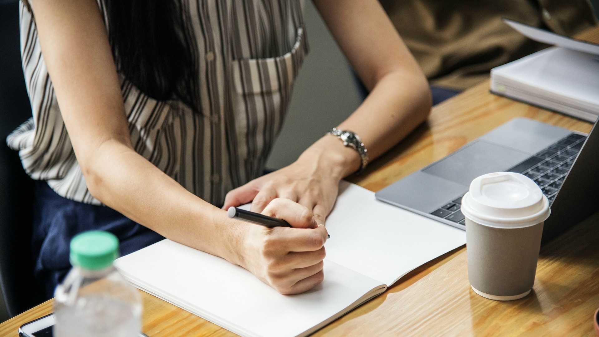woman taking notes at a laptop with a cup of coffee