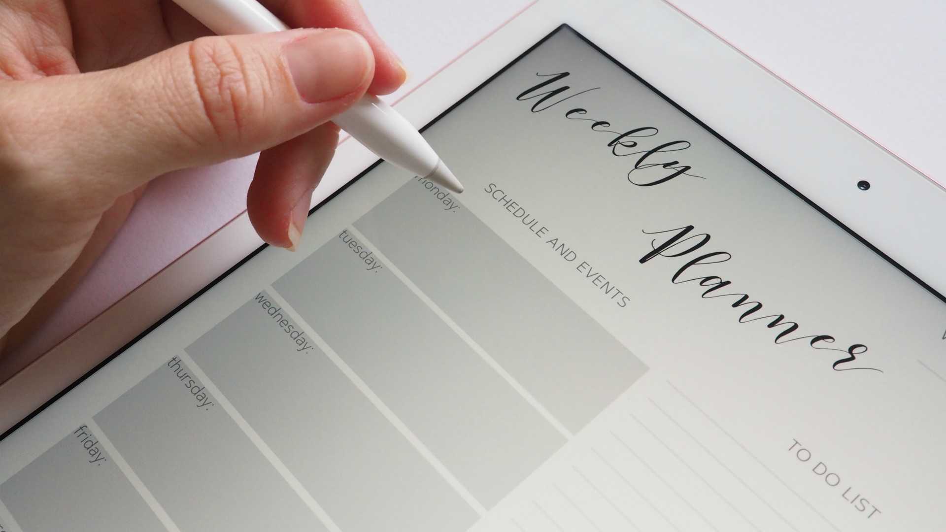person writing on a weekly planner tablet with a stylus