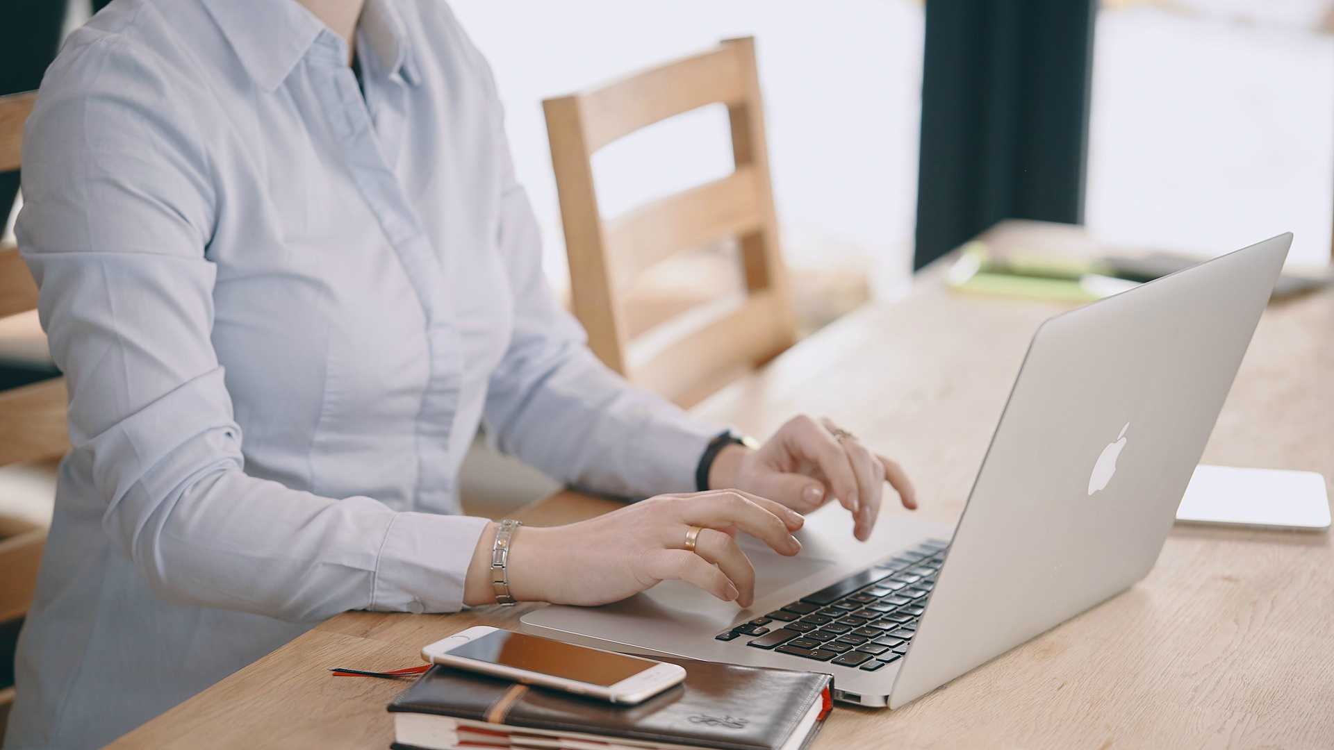 woman working on a laptop with a notebook and phone next to her