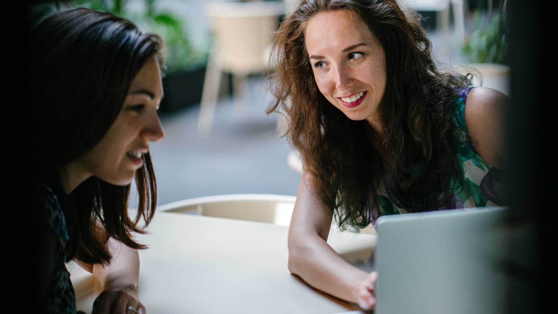 one woman helping another woman on a laptop
