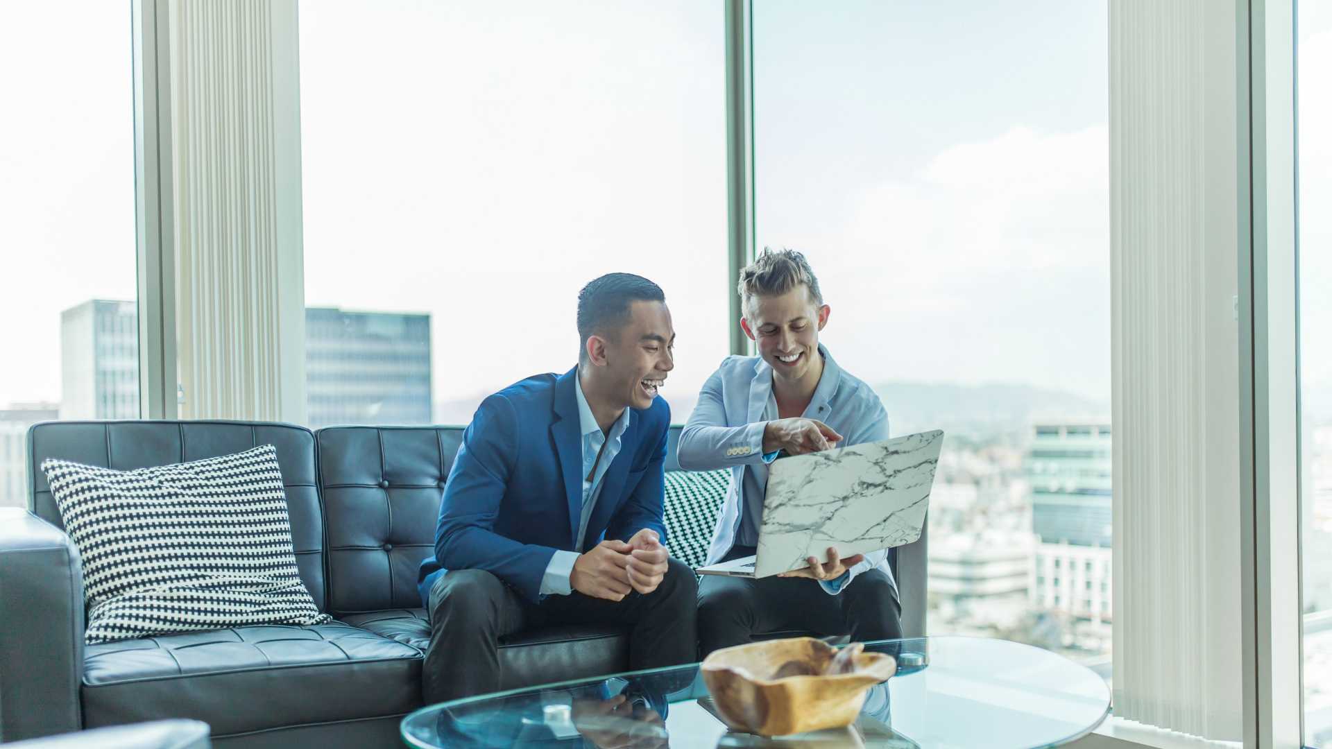 two men looking at a laptop on an office couch