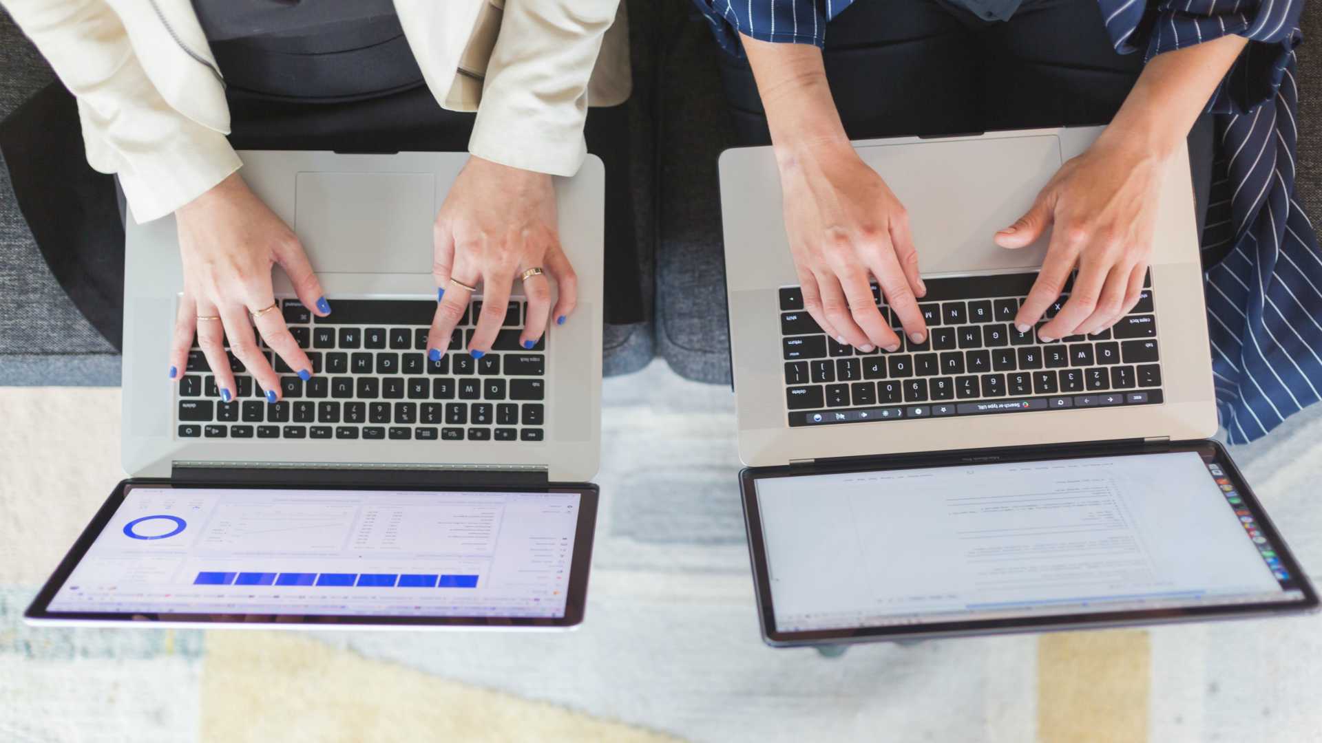 two co-workers sitting on a couch working on laptops