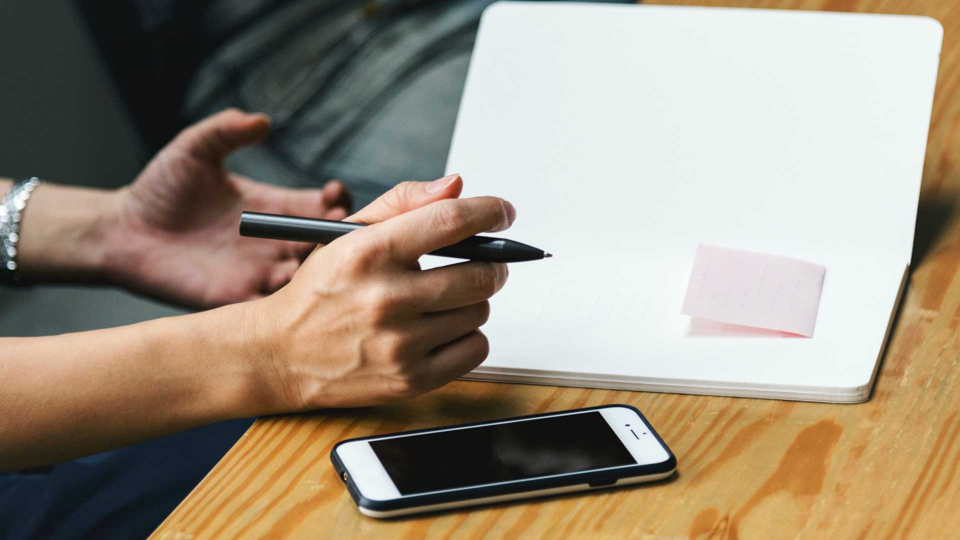 person taking notes in a notebook with a smartphone