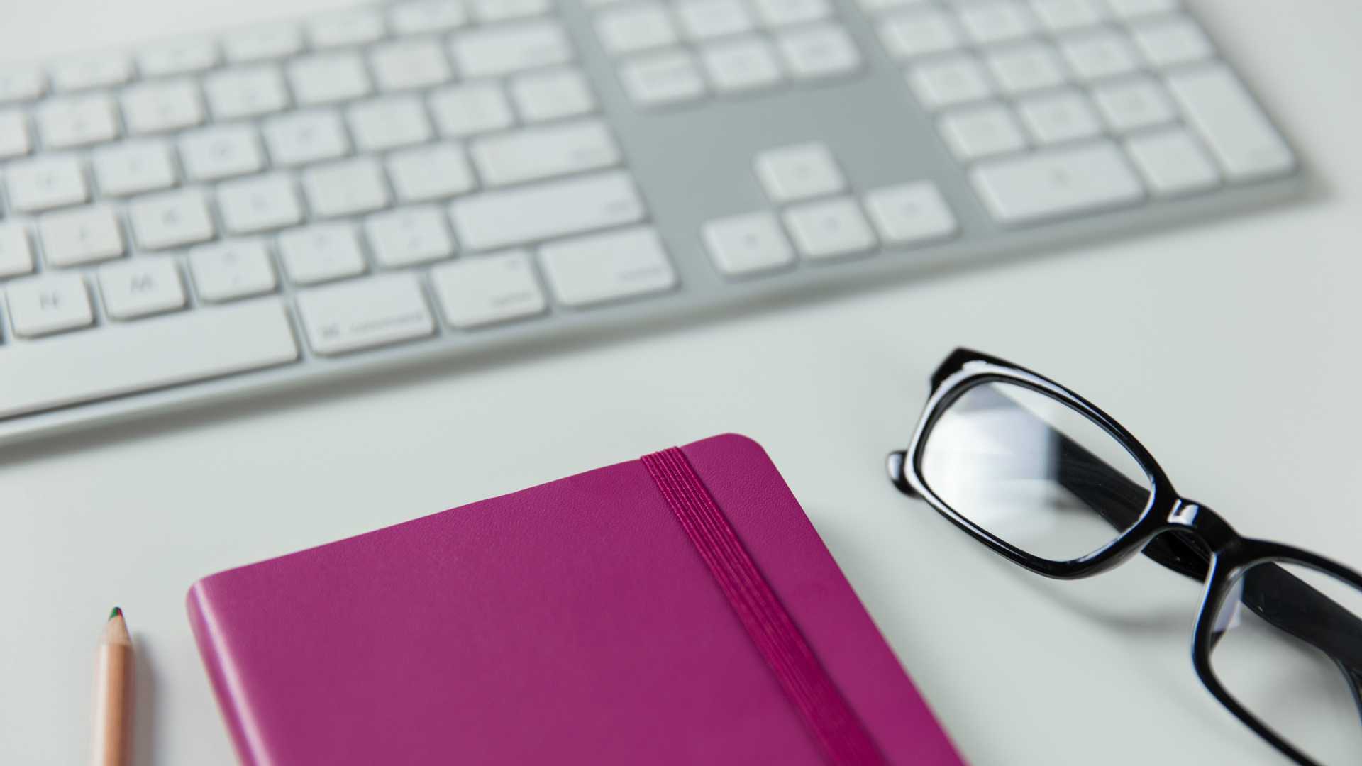 keyboard, notebook, pencil and glasses on a desk