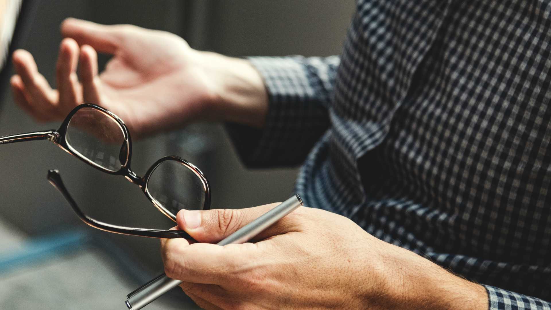 man talking and holding his glasses