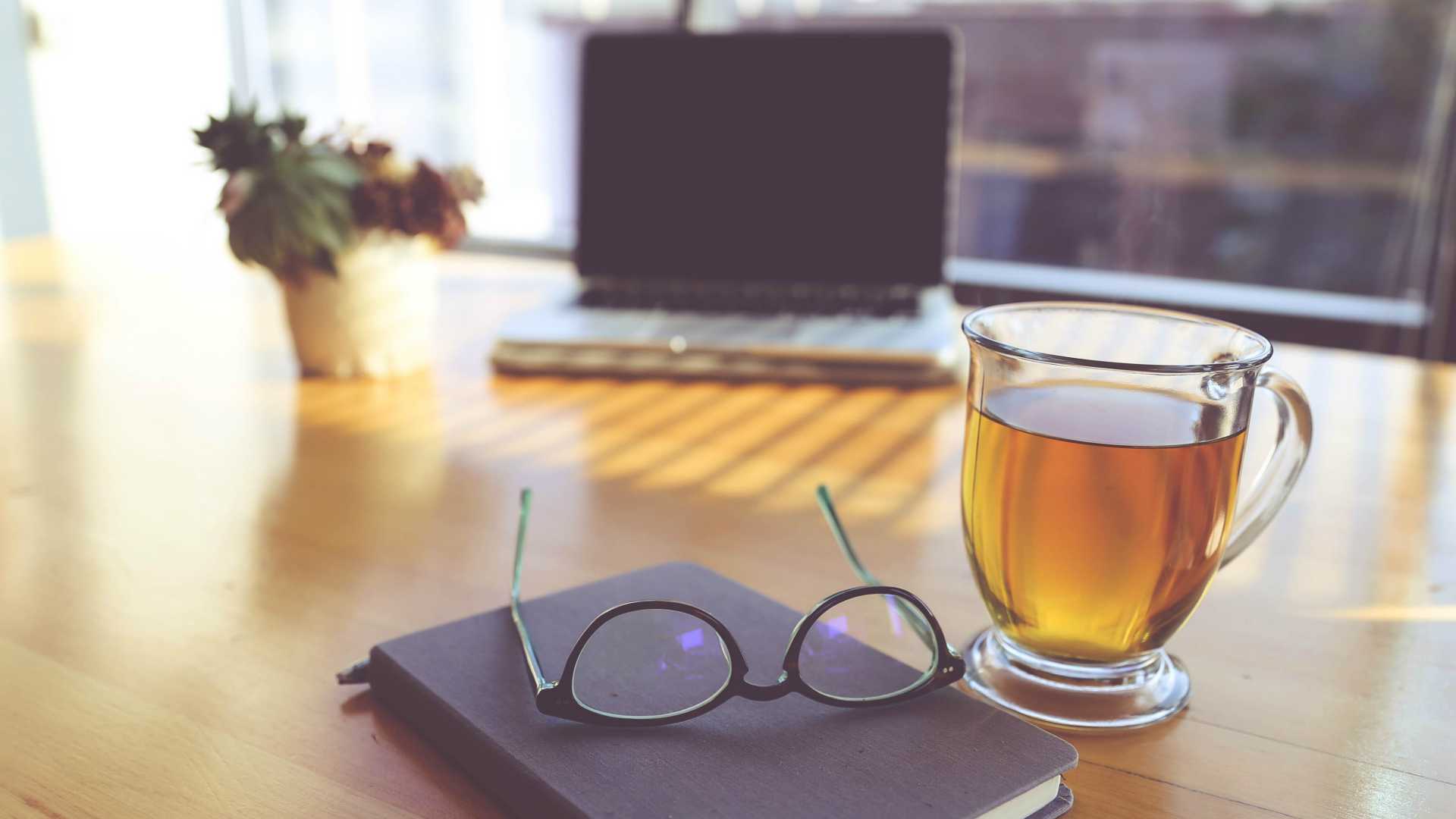 desk with plant, laptop, notebook, glasses and tea