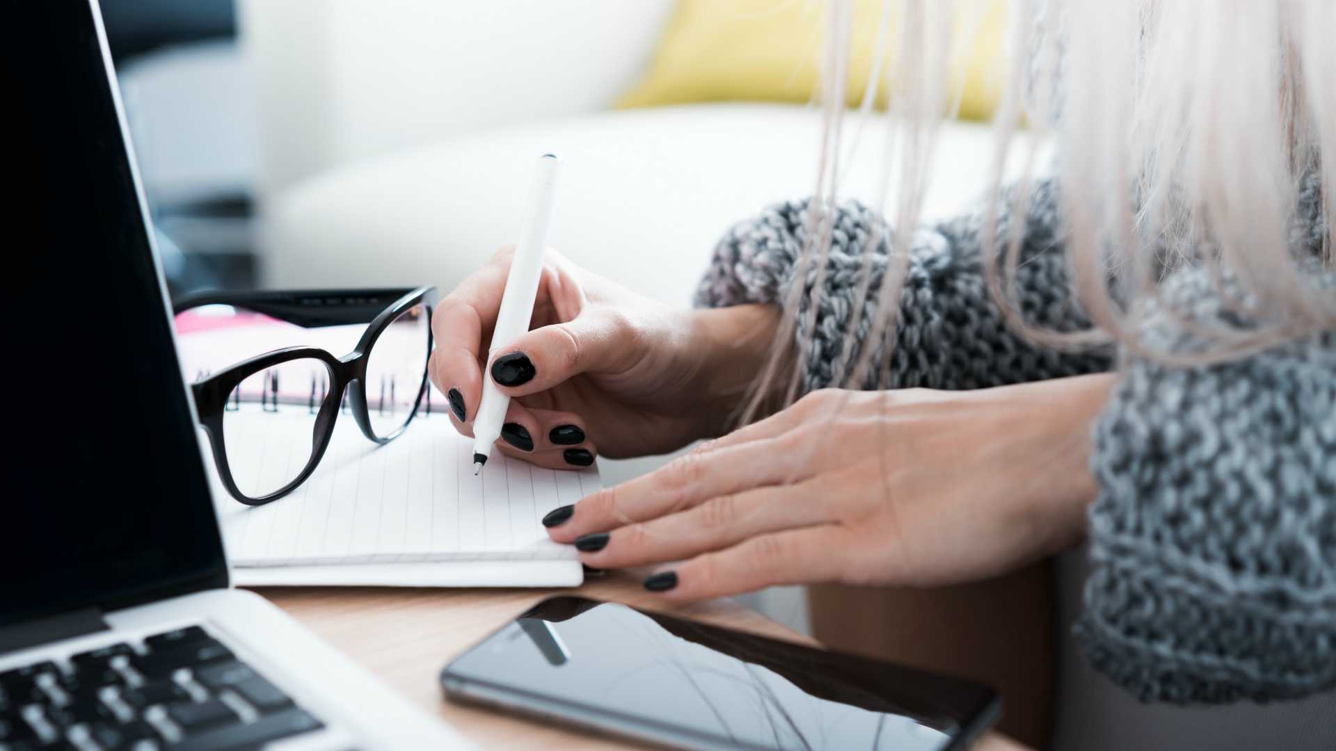 woman taking notes at a desk with a laptop and a smartphone