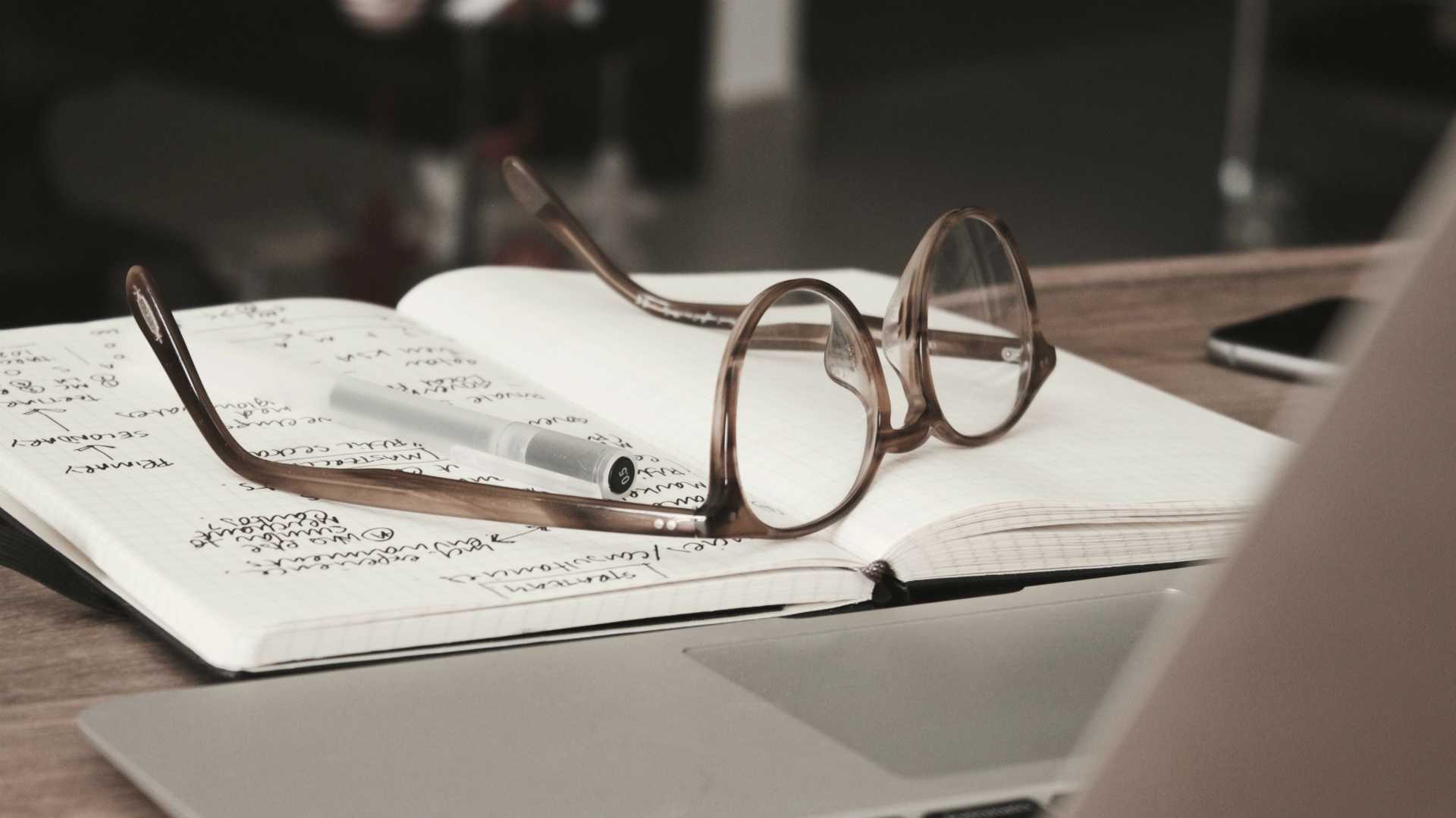 glasses on top of a notebook in front of a laptop