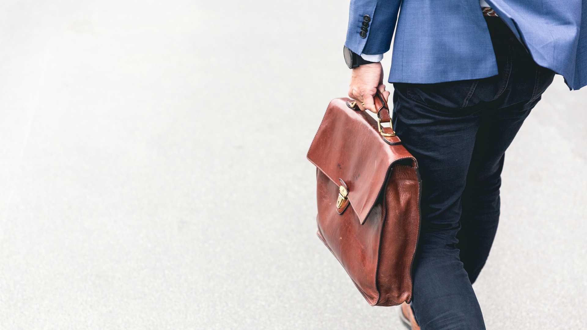 man walking away from the camera holding a briefcase and wearing a blazer