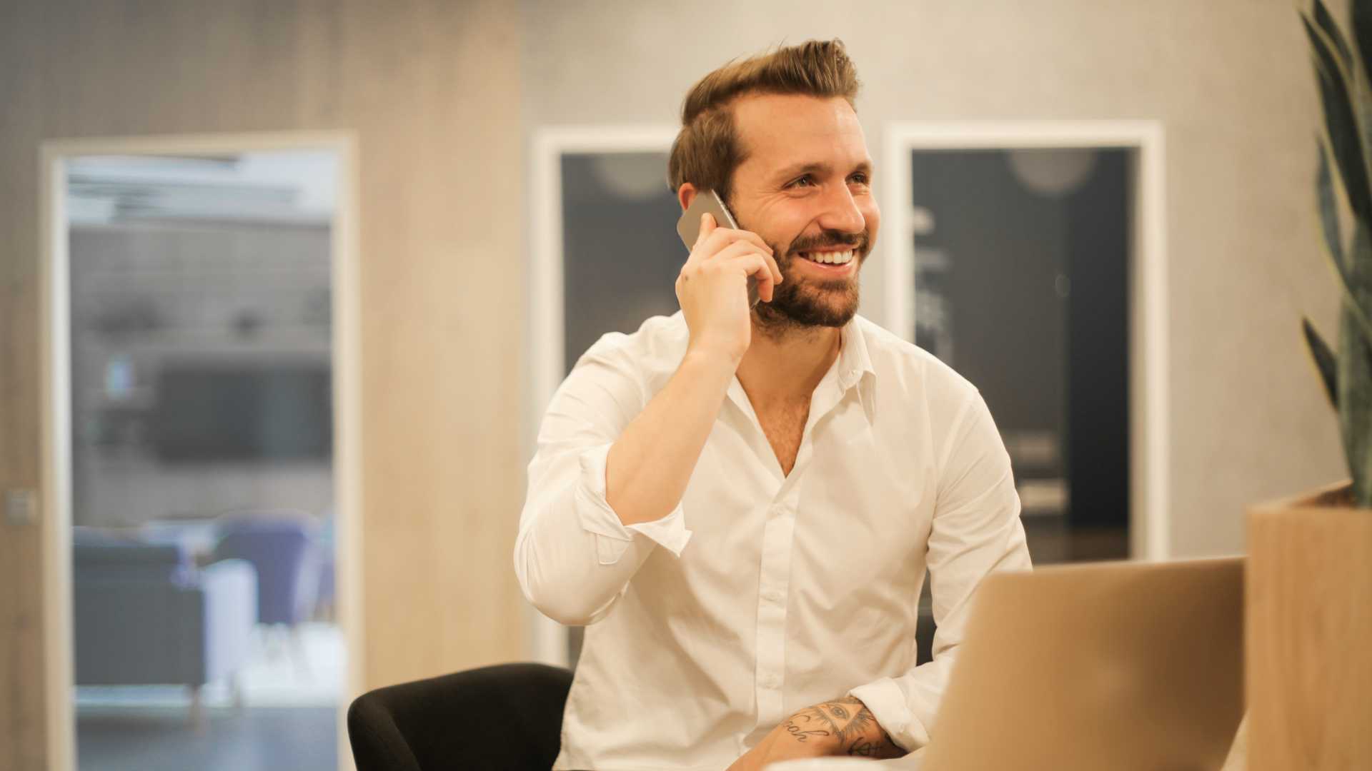 businessman talking on his smartphone; laptop sitting on his desk