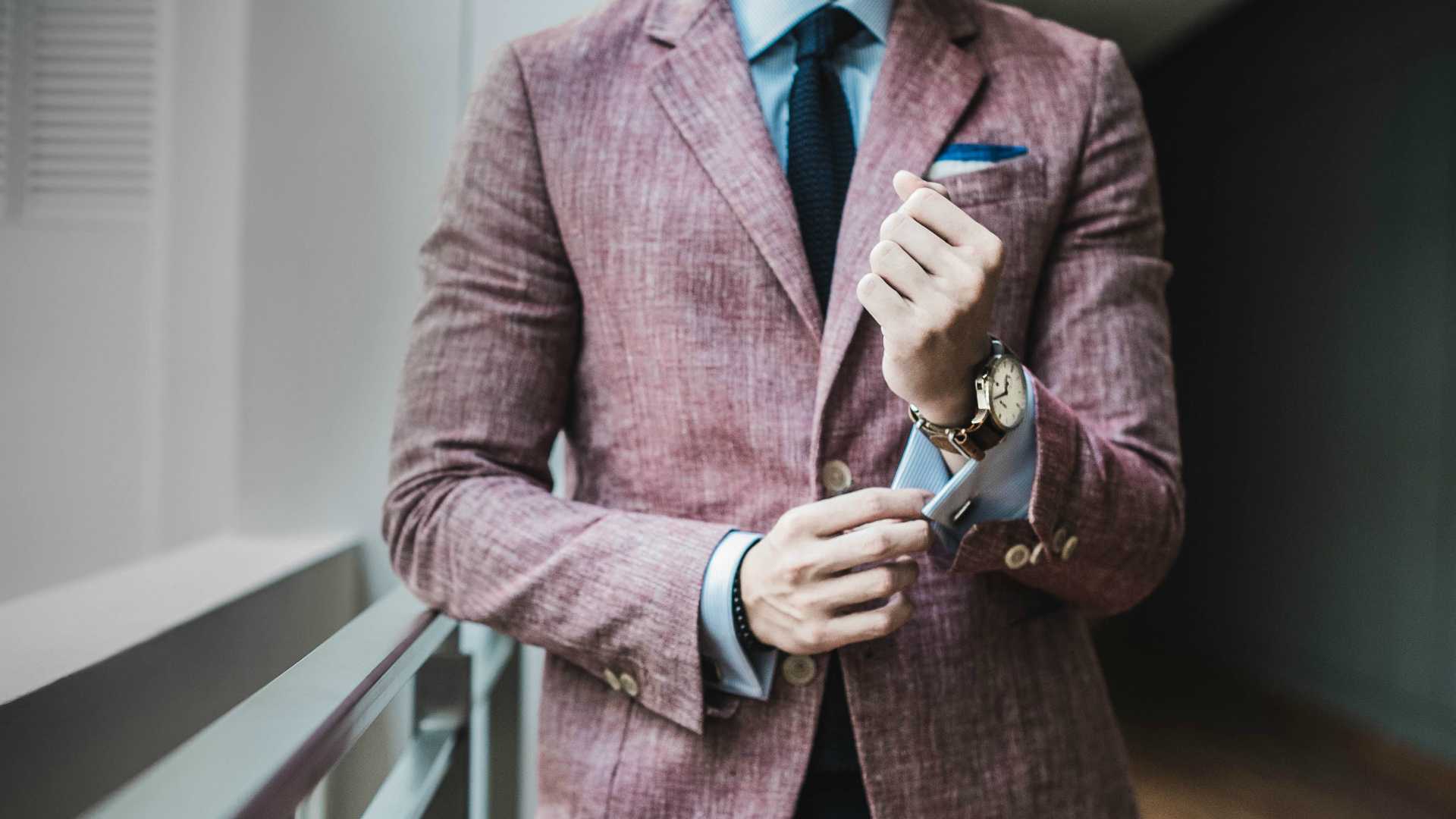 man in a pink suit buttoning his sleeve button and walking toward the camera