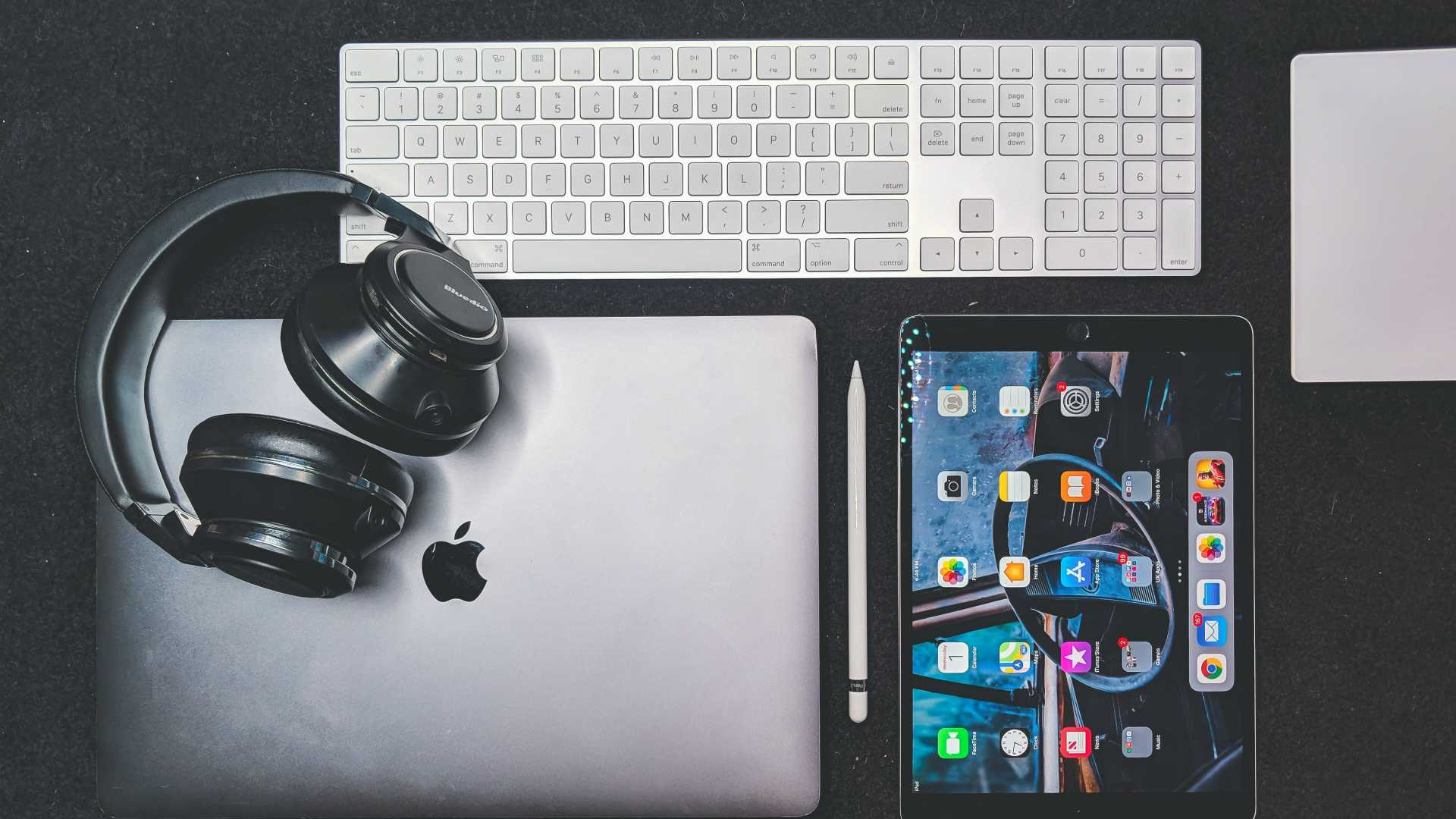 table with a computer keyboard, a laptop, a tablet and headphones