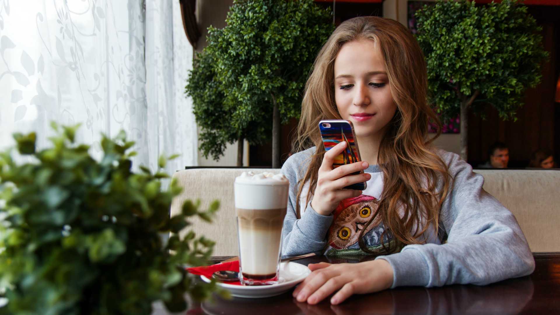 teenage girl using a smartphone at a table with plants and a milkshake
