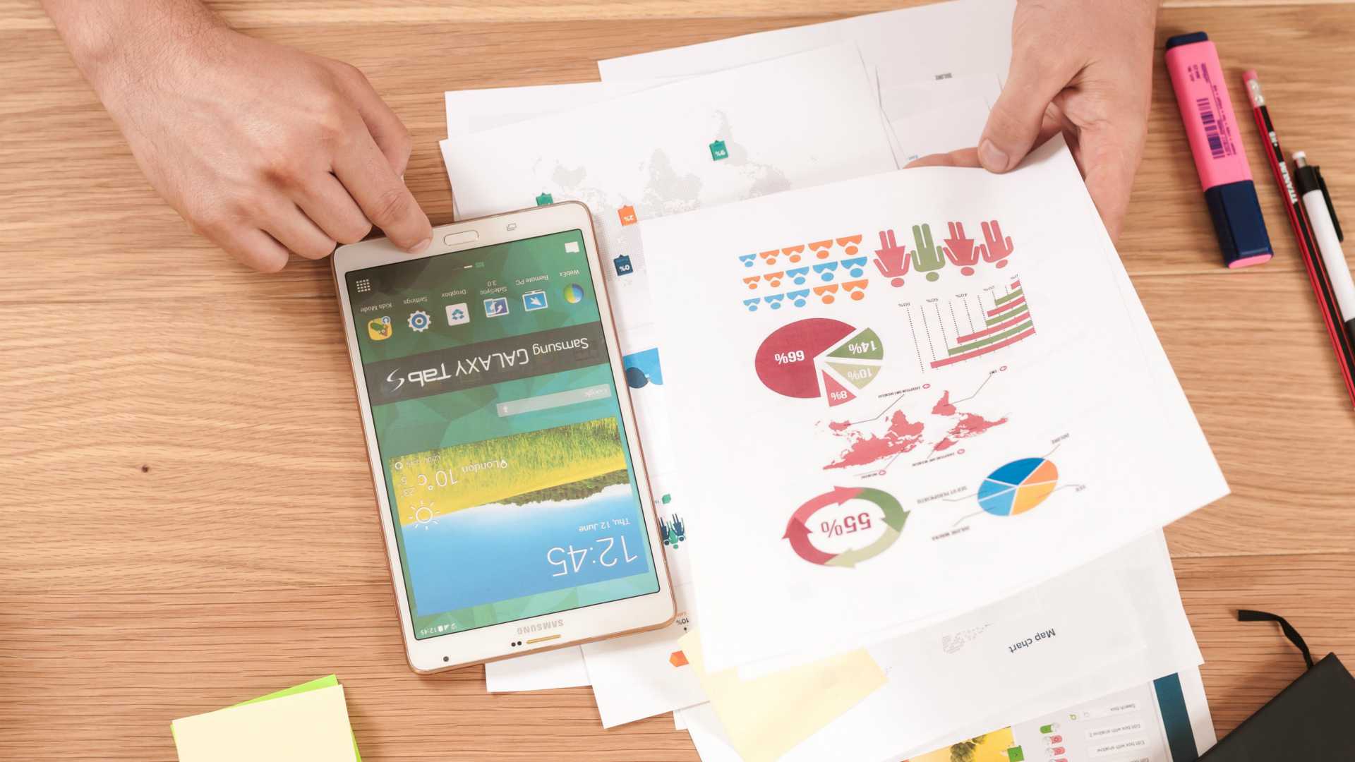 man's hands at a table looking through charts; a smartphone and highlights are on the table