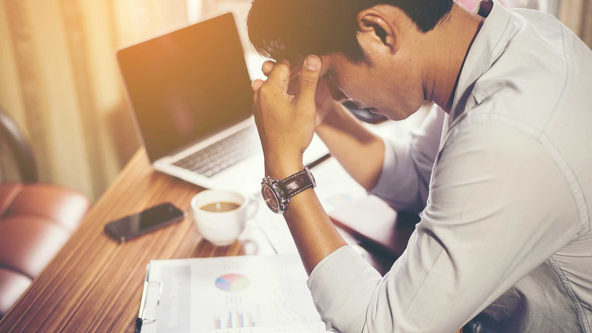 stressed man sitting at a desk with his head in his hands