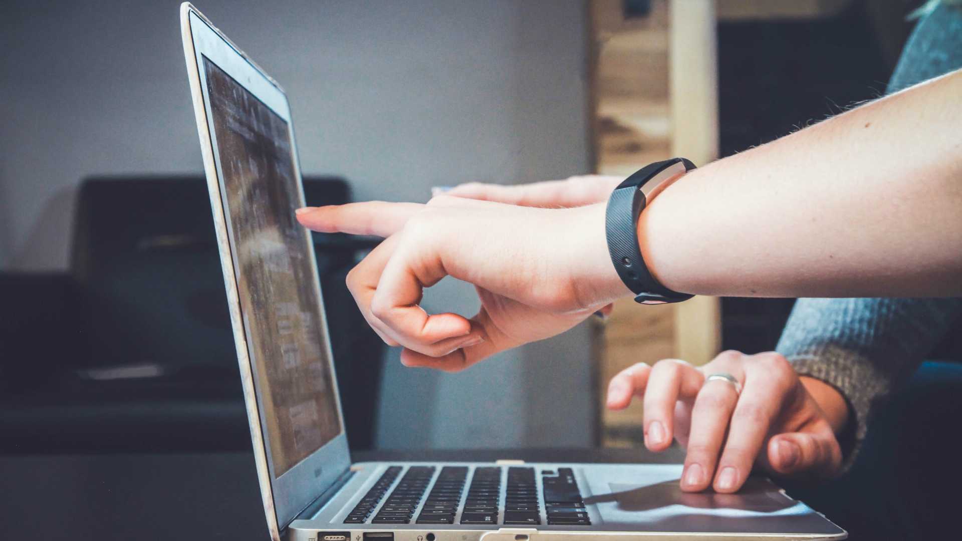 hands of two people working on a laptop; one is pointing, the other is using the mousepad