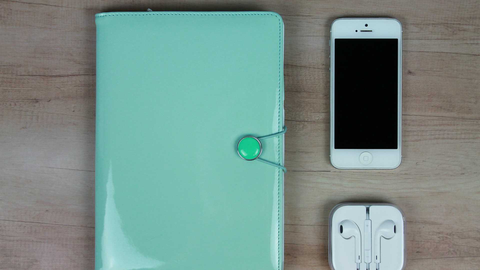 table with a planner or notebook, smartphone and earbuds on it