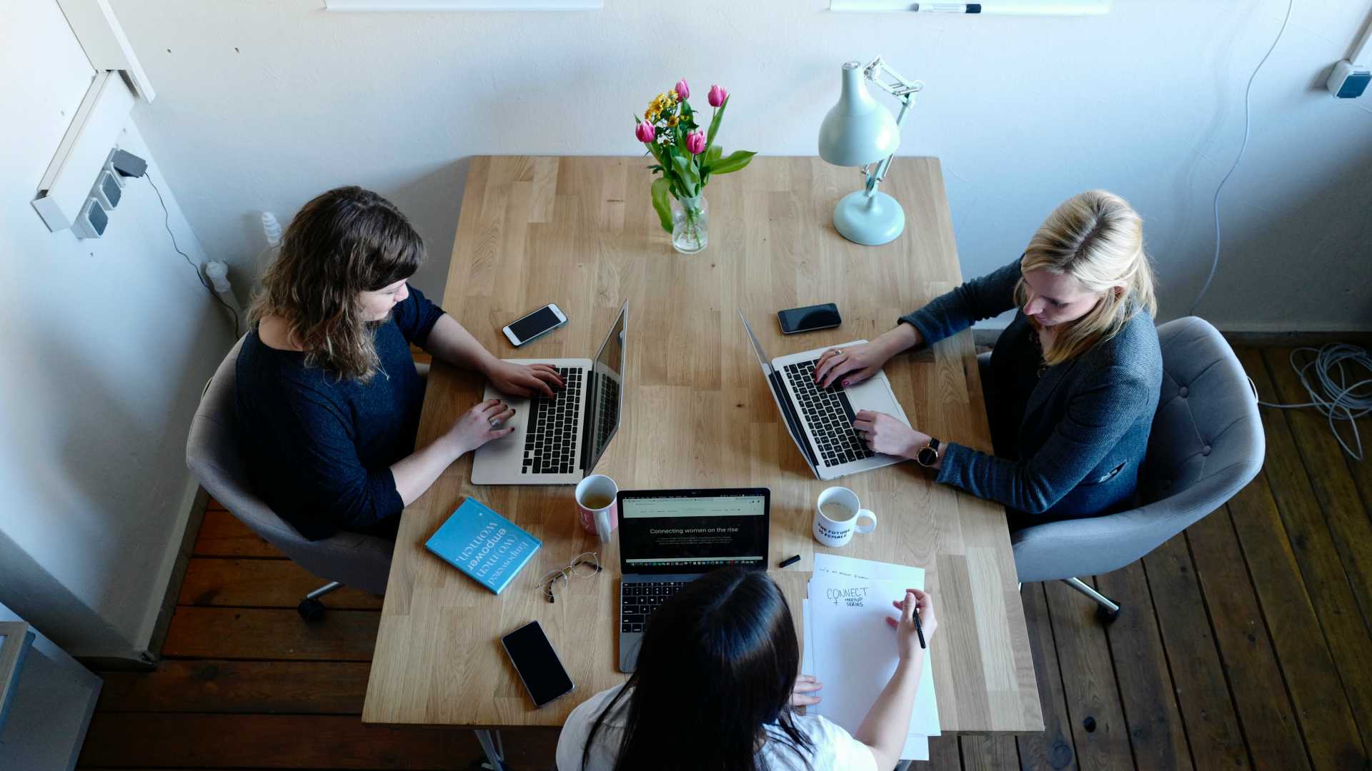 three young women working at a table with laptops and notebooks