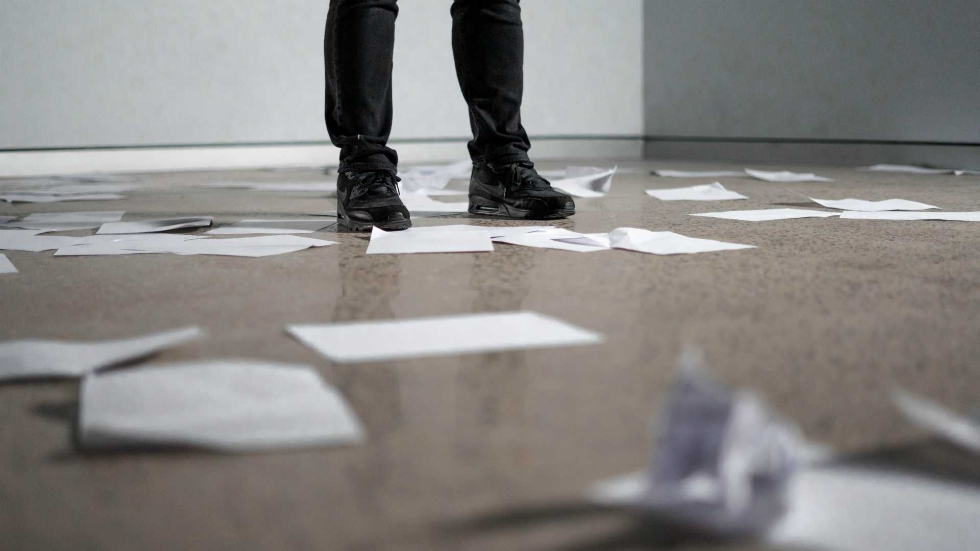 man's feet standing on a paper cluttered with paper, some crumpled