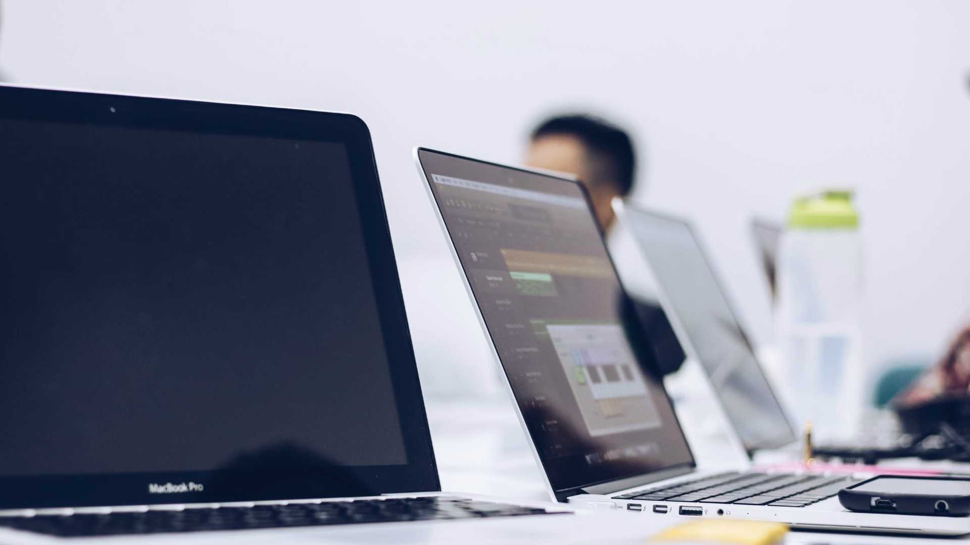 three laptops on a table, with a couple people sitting at the table but mostly cut out of the photo