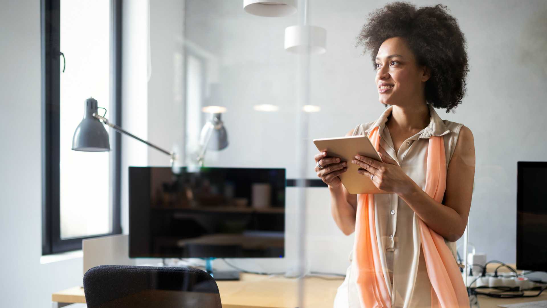 young black female leader in her office, holding a tablet and looking out the window
