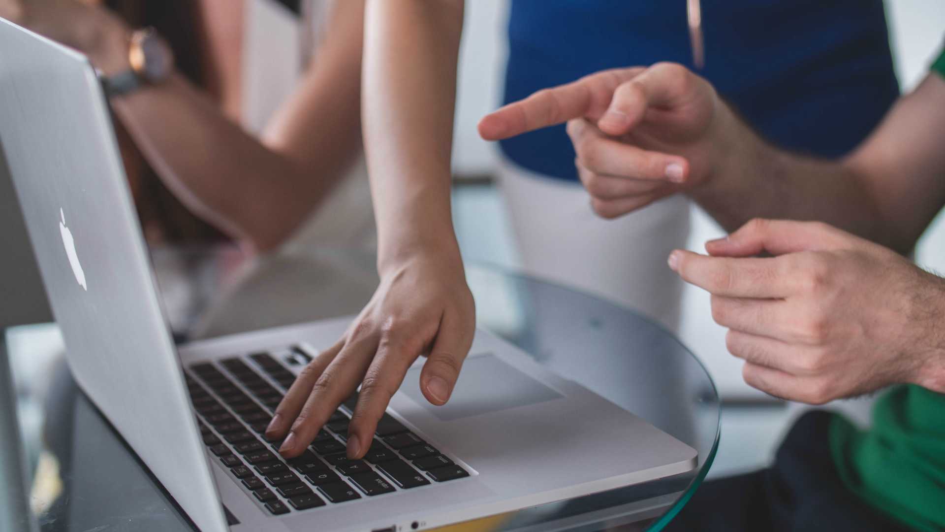 woman's hand typing on a laptop to assist a man, who is pointing at the laptop screen
