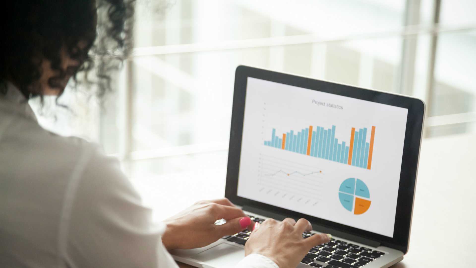 view from behind of a woman sitting at a desk and looking at charts on her laptop