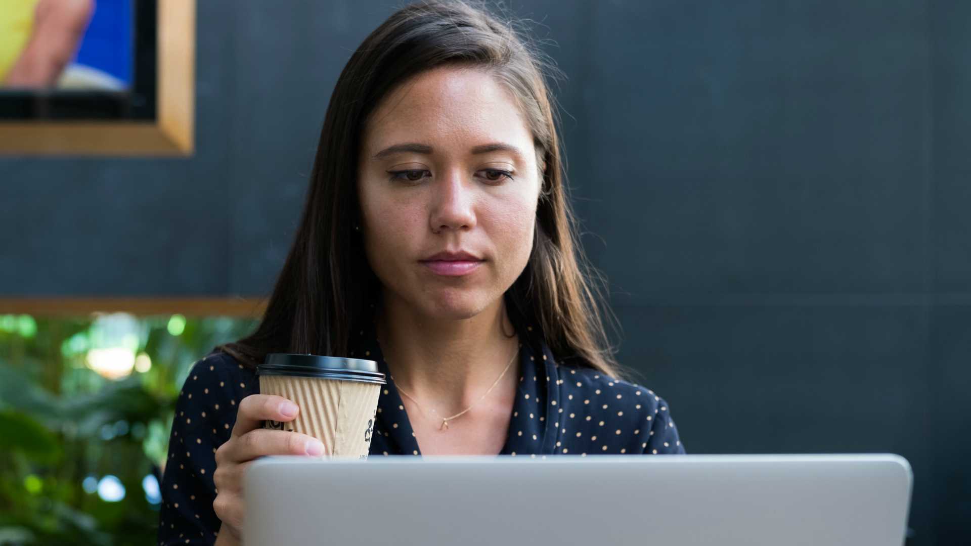 young woman drinking coffee and looking at a laptop