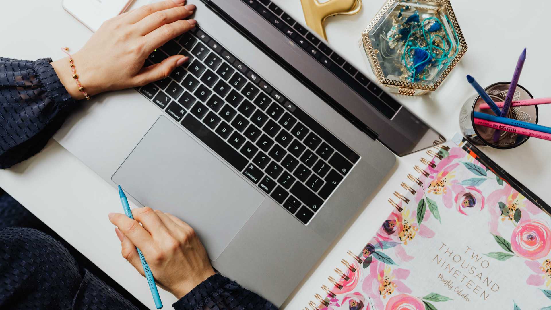 woman using her laptop; 2019 planner next to her on her desk, along with cups of pencils and paper clips