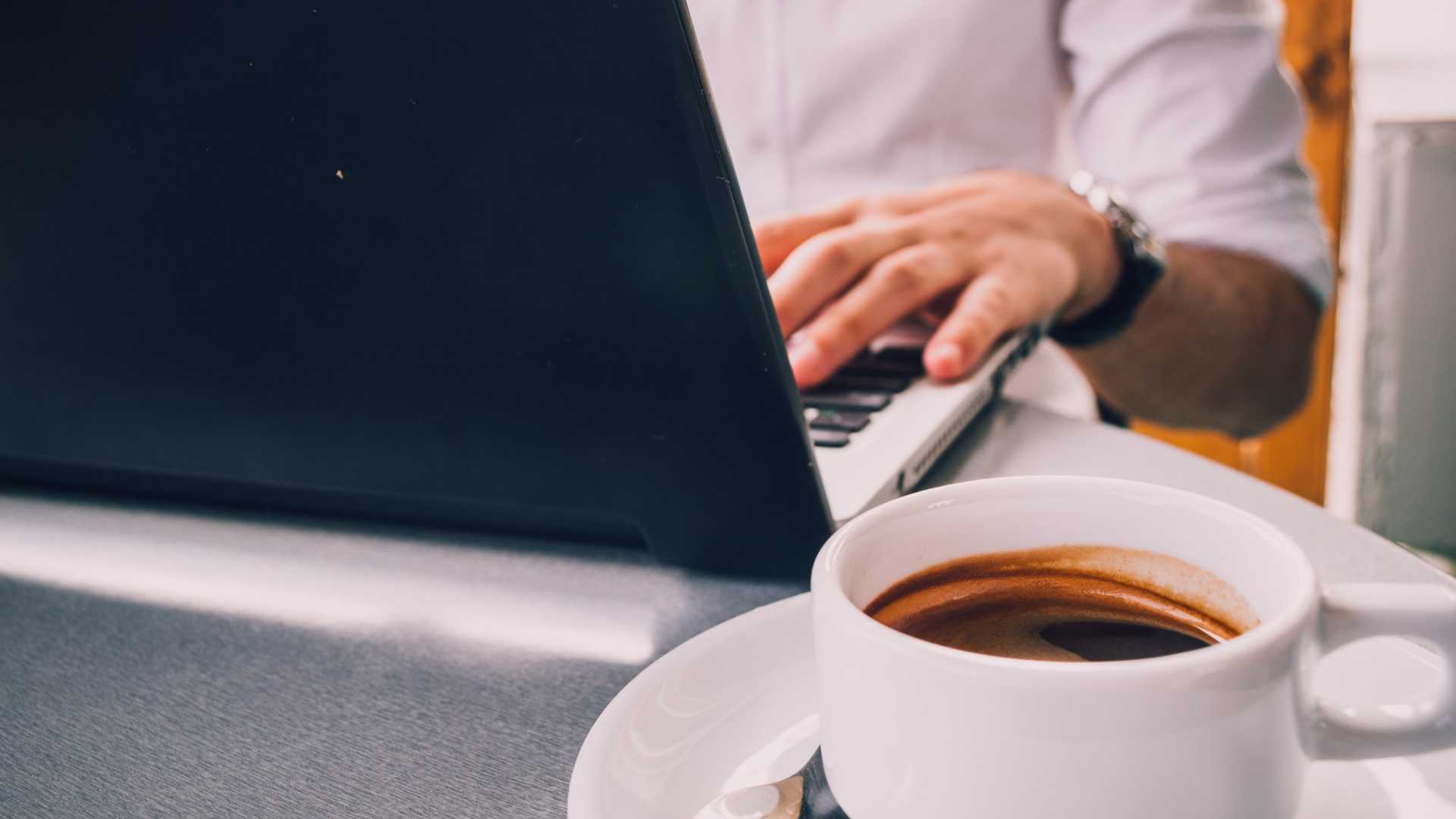 man's hands typing on a laptop; cup of coffee on the table