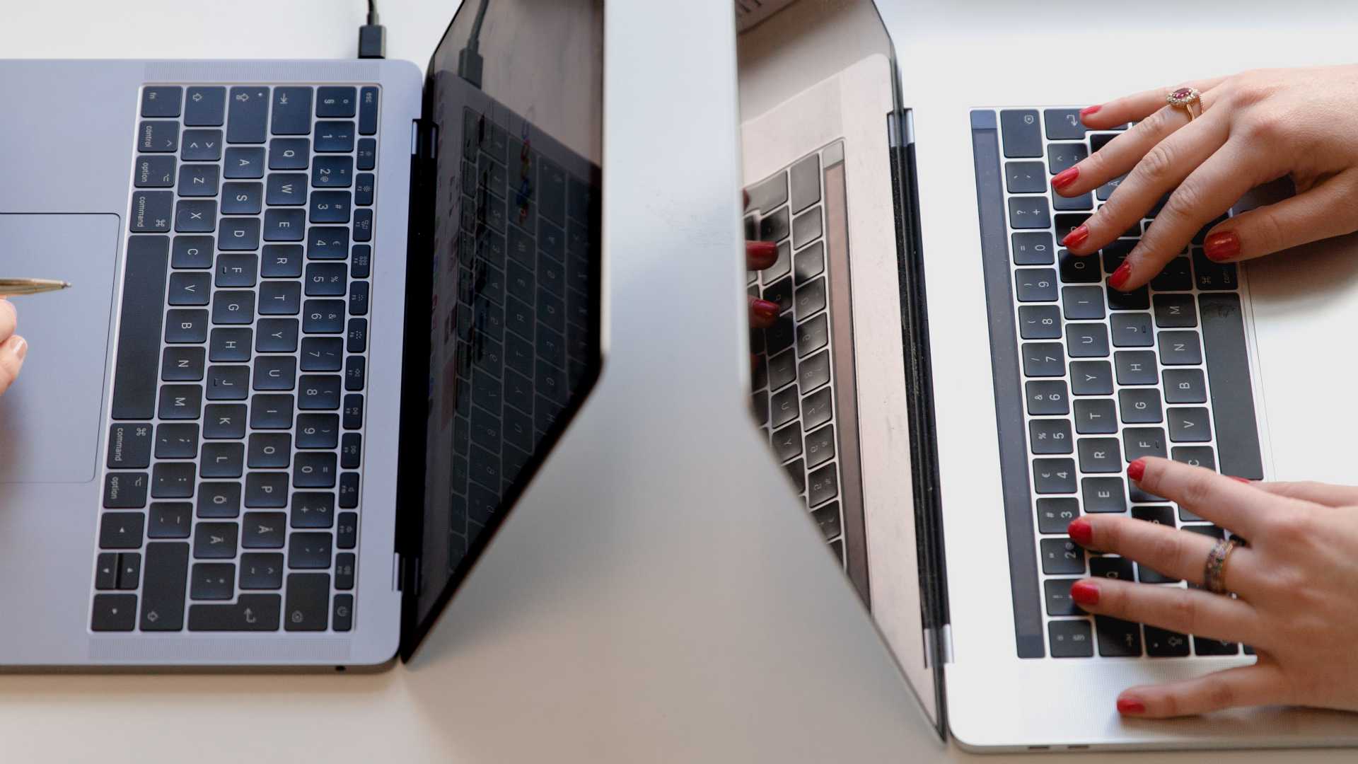 two women's hands typing on laptops facing each other