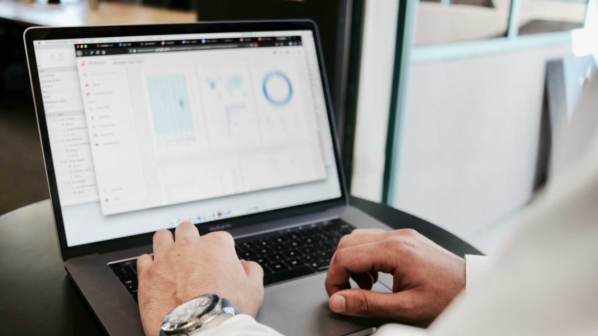 man's hands typing on a laptop with charts on the screen
