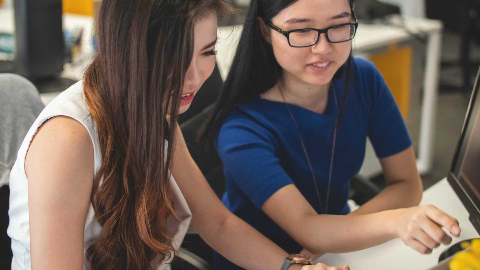 two young women at work; one is pointing at a computer screen