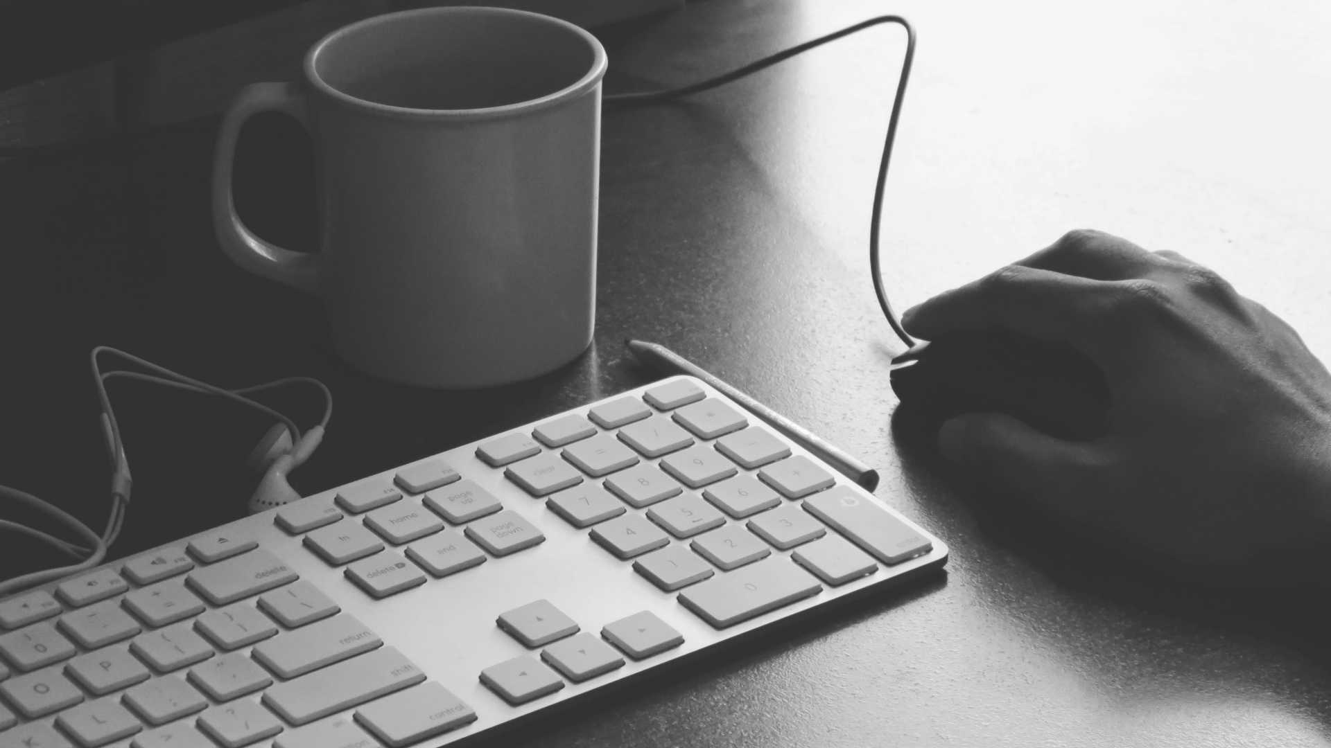 hand clicking a mouse; keyboard and coffee mug are on the desk