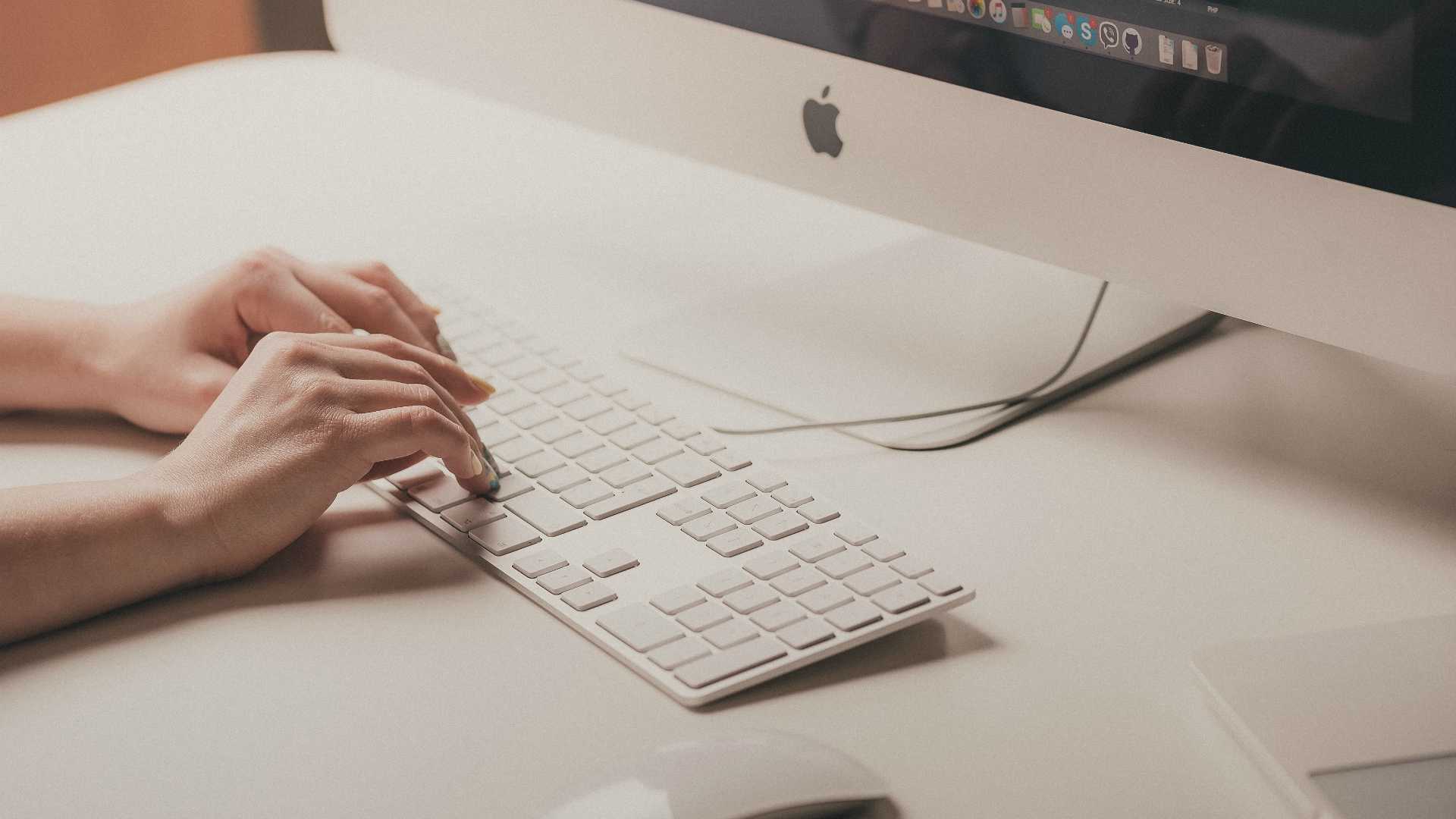 woman's hands typing on a keyboard; social/communication apps are visible on the monitor