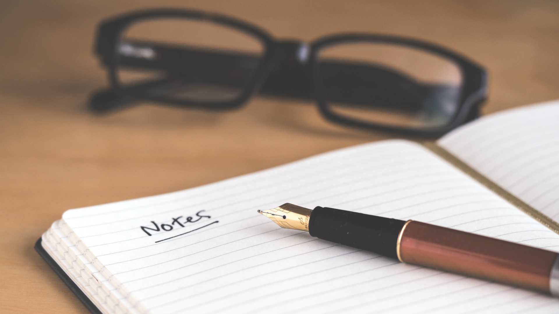 glasses, open notebook with "Notes" written at the top of a page, and pen