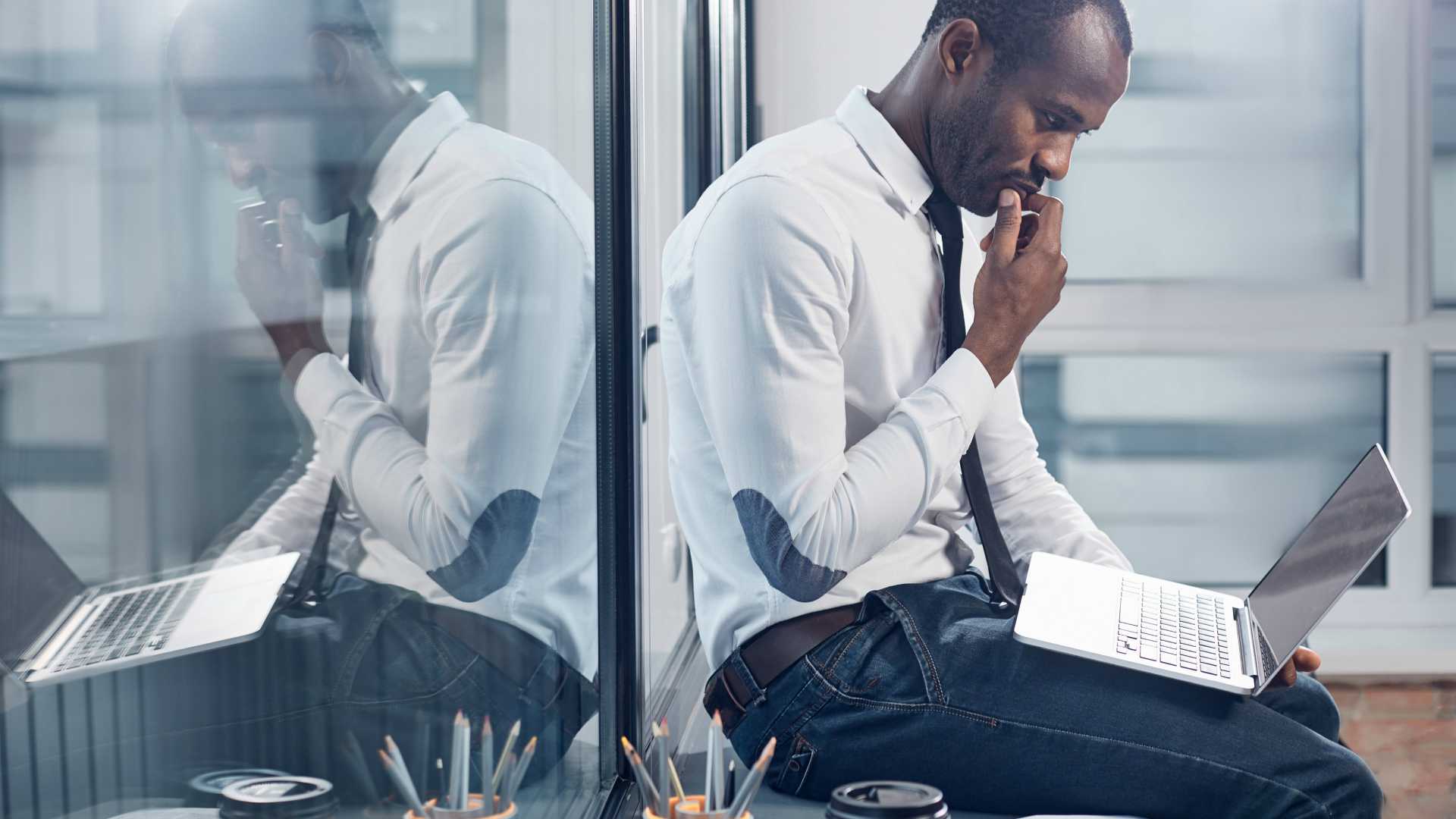 African American businessman sitting on windowsill and working on laptop