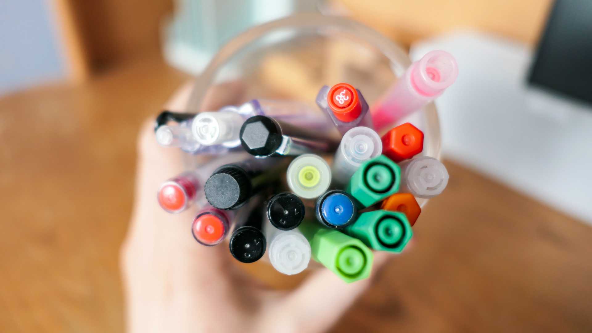 hand holding a cup of different colored pens