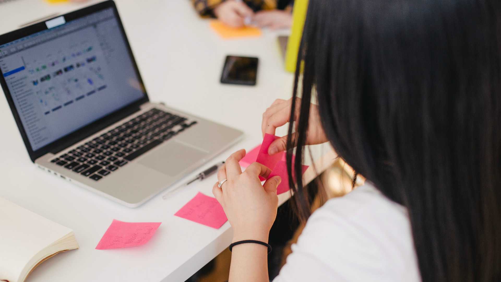 Business woman writing reminders on sticky notes and working on laptop