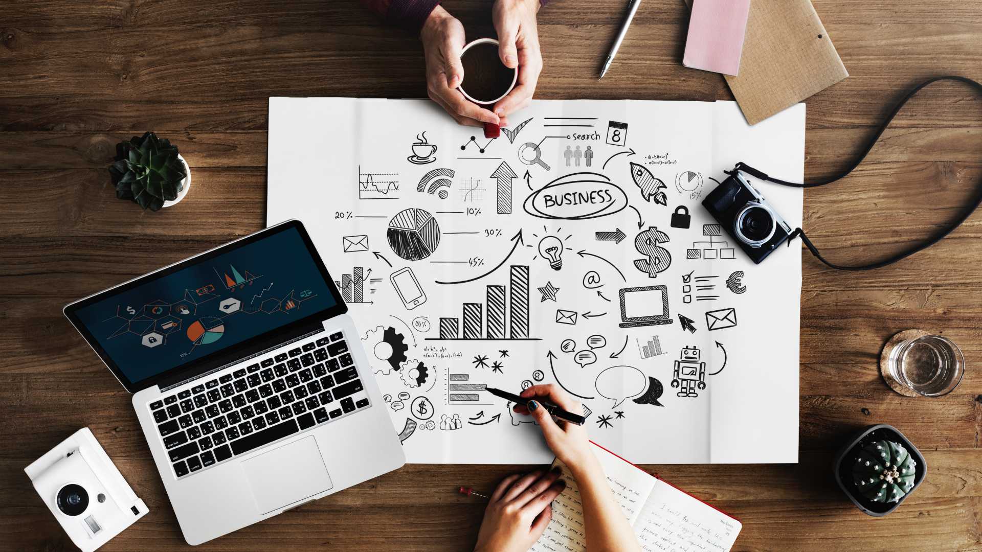 two people meeting with a large business graphic, a laptop, a camera and notebooks